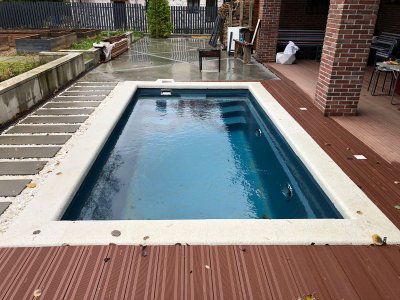 Прямоугольный бассейн с темной внутренней отделкой на заднем дворе с террасной доской